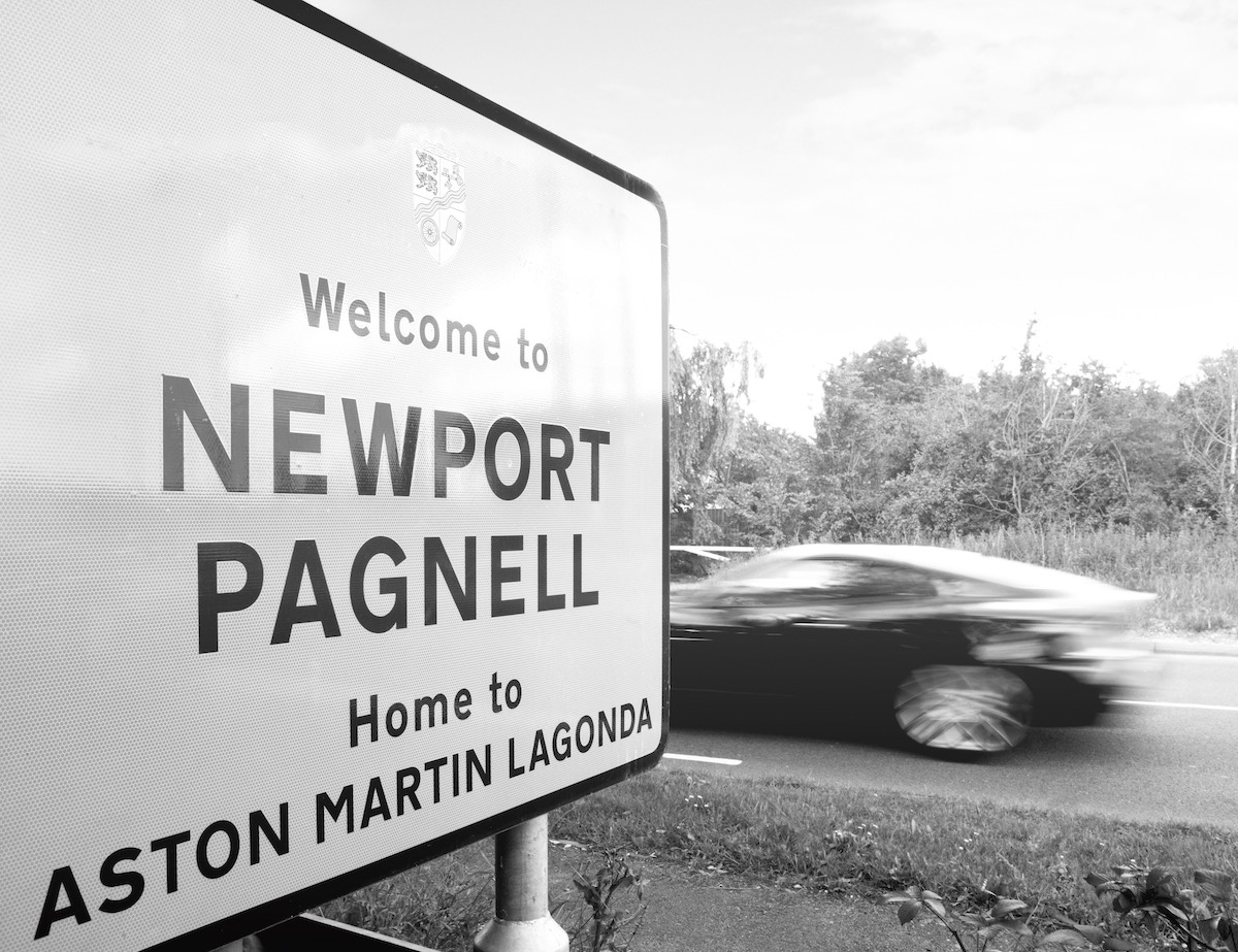 Aston Martin driving past the Newport Pagnell sign