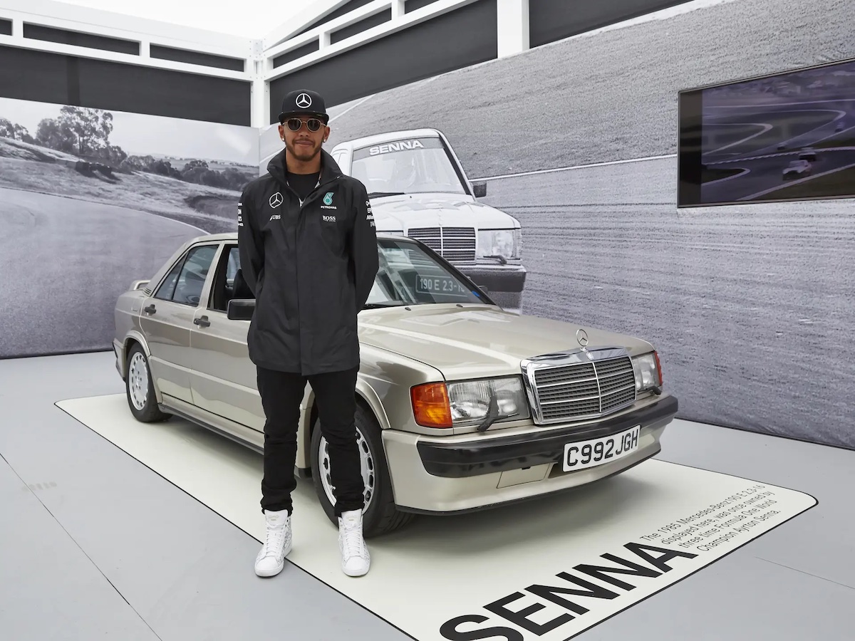Lewis Hamilton standing next to 1985 Mercedes-Benz 190 E 2.3-16 once owned by Ayrton Senna