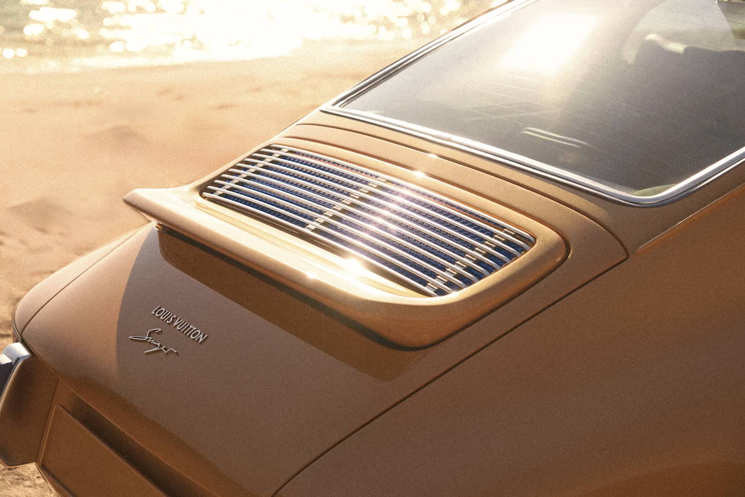 Detail of rear engine cover showing speed-activated spoiler above Louis Vuitton and Singer emblems.